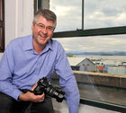 Dave Abrams standing in front of a window overlooking Lake Champlain with a camera