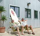 Dave Schmidt and Tom Pasley sitting in the sun in front of a surfboard
