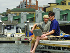 Mike McCarney and Ben Ipsen sitting on the pier with a laptop in front of main street landing