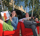 Nicole Ravlin and Ken Liatsos sitting in red chairs reading magazines